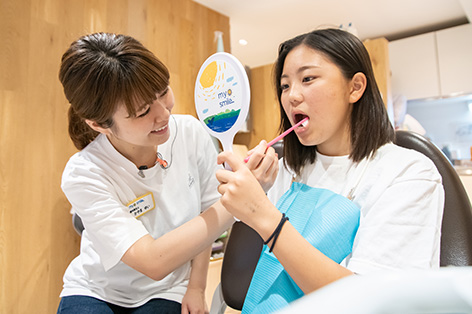 10代の女性に歯磨きのコツを教えるスタッフ