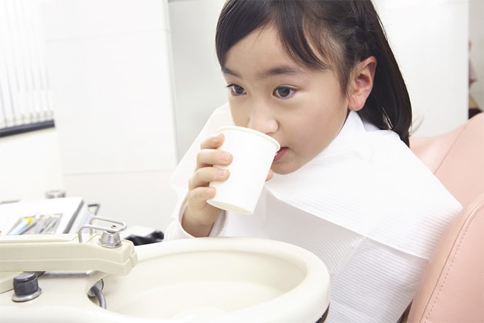 歯科医院で白い紙コップを手に持ち、うがいをしようとしている女の子
